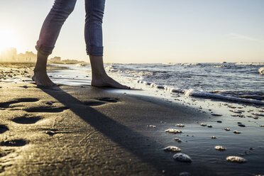 Beine einer barfüßigen Frau, die am Strand am Wasser steht, Riccione, Emilia-Romagna, Italien - CUF08440