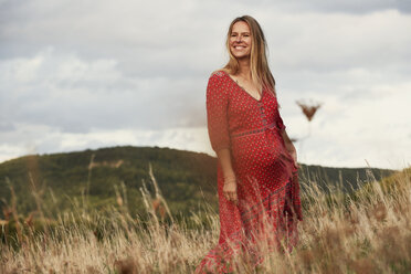 Porträt einer glücklichen schwangeren Frau im roten Kleid auf einem Hügel - CUF08449