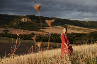 Portrait of happy pregnant woman in red dress on hillside - CUF08450