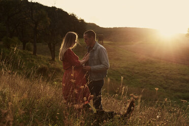 Romantic mid adult pregnant couple face to face on hillside at sunset - CUF08451