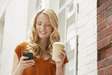 Woman having coffee and texting in street, London, UK - CUF08456