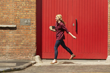 Woman walking past red door, London, UK - CUF08461