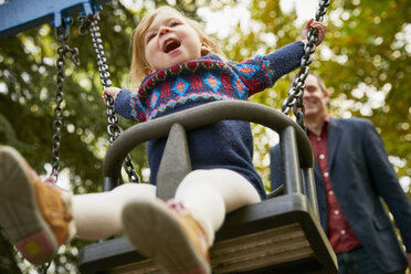 Father pushing daughter on playground swing - CUF08502