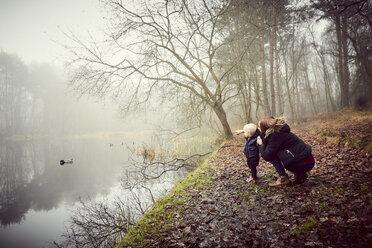 Mid adult woman crouching with toddler son on misty riverbank - CUF08513