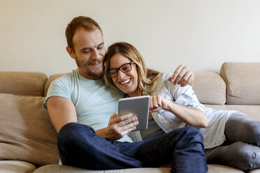 Mid adult couple relaxing on sofa, looking at digital tablet - CUF08565