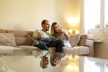 Mid adult couple relaxing on sofa, looking at smartphone - CUF08566