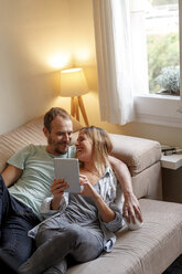 Mid adult couple relaxing on sofa, looking at digital tablet - CUF08567