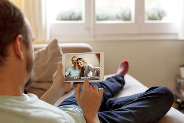 Mann sitzt auf dem Sofa und betrachtet Fotos auf einem digitalen Tablet, Rückansicht - CUF08568