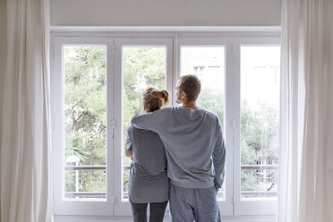 Mid adult couple at home, looking out of window, man hugging woman, rear view - CUF08575