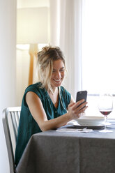 Frau sitzt an einem Tisch im Diner, benutzt ein Smartphone, lächelt - CUF08579