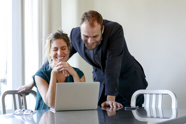 Mid adult couple at home, woman using laptop, man looking over her shoulder - CUF08581