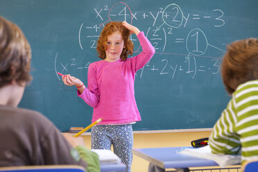 Grundschülerin kratzt sich am Kopf über die Gleichung an der Tafel im Klassenzimmer - CUF08583