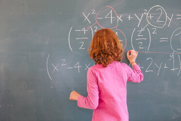 Rückansicht einer Grundschülerin, die eine Gleichung an der Tafel im Klassenzimmer löst - CUF08584