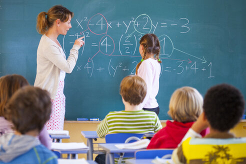 Grundschullehrer, der eine Gleichung an der Tafel im Klassenzimmer erklärt - CUF08585