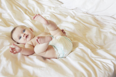 Portrait of cute blue eyed baby girl in diaper lying on bed - CUF08604
