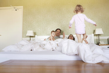 Female toddler stepping on bed with parents and baby sister - CUF08606