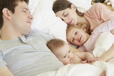 Ein kleines Mädchen und seine kleine Schwester kuscheln im Bett mit ihren schlafenden Eltern - CUF08609