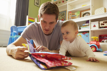 Mid adult man and baby daughter reading storybook in playroom - CUF08614