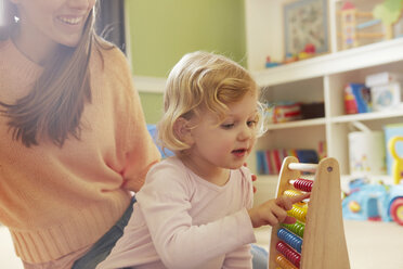 Mid adult woman and toddler daughter counting on abacus in playroom - CUF08615