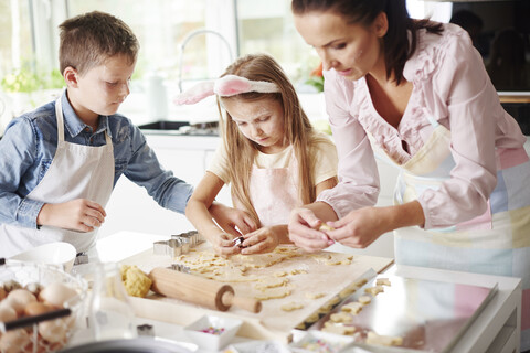 Mädchen, Bruder und Mutter backen Osterplätzchen am Küchentisch, lizenzfreies Stockfoto