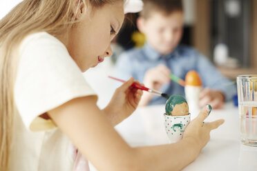 Mädchen malt hartgekochte Ostereier am Tisch grün an - CUF08658