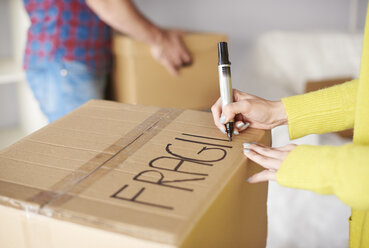 Young couple moving home, young woman labelling cardboard box, mid section - CUF08659