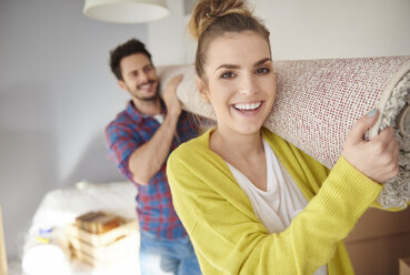 Young couple moving home, carrying rolled tug on shoulders, smiling - CUF08662