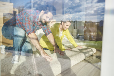 Junges Paar beim Ausrollen des Teppichs im neuen Haus, Blick durch das Fenster - CUF08663