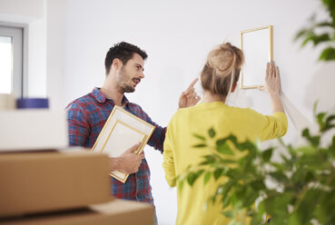 Young couple in new home, putting picture on wall - CUF08669