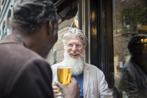 Zwei reife Männer, die vor einer Kneipe stehen und Bier trinken - CUF08691