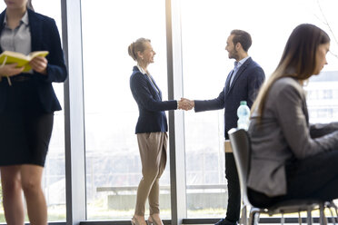 Businesswoman and man shaking hands by office window - CUF08693