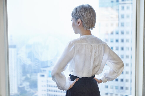 Rear view of businesswoman, hands on hips, looking out of window - CUF08760