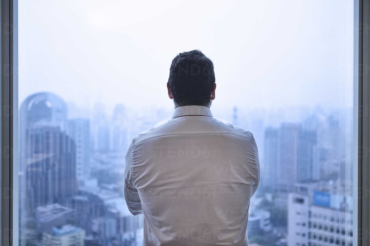Man looking through window at cityscape stock photo - OFFSET