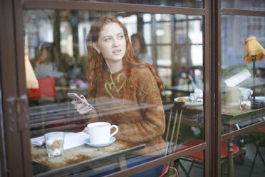 Blick durch das Fenster einer Frau in einem Café, die ein Mobiltelefon benutzt - CUF08768