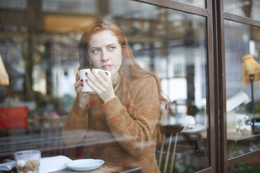 Blick durch ein Fenster auf eine Frau in einem Café, die eine Tasse hält - CUF08771