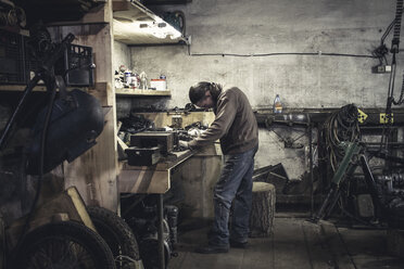 Mechaniker bei der Arbeit an einer Werkbank mit zerlegtem Oldtimer-Motorrad in der Werkstatt - CUF08784