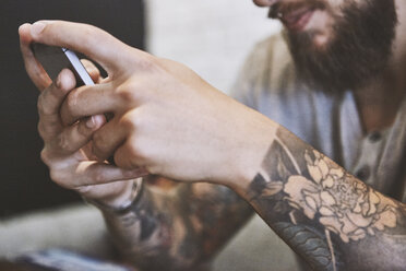 Hands of tattooed young male hipster holding smartphone, close up - CUF08849