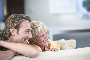 Father and son relaxing on sofa, looking away smiling - CUF08859