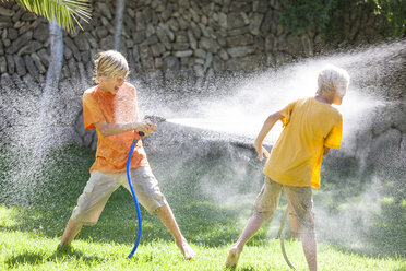 Boys in garden spraying each other with water from hosepipe - CUF08864