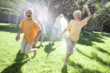 Eltern bespritzen ihre Söhne im Garten mit Wasser aus einem Schlauch - CUF08865