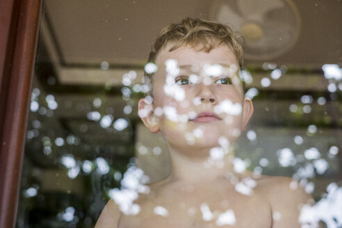 Porträt eines nachdenklichen Jungen hinter einer Fensterscheibe mit Blick in die Ferne - MMIF00062