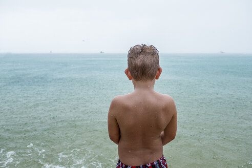 Back view of boy standing in front of the sea on rainy day - MMIF00064