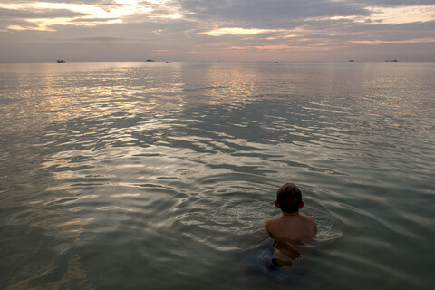 Thailand, Junge schwimmt bei Sonnenuntergang im Meer, lizenzfreies Stockfoto