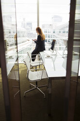 Geschäftsfrau mit Mobiltelefon am Bürofenster, London, UK - CUF08961