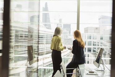 Geschäftsfrauen im Gespräch am Fenster im Büro, London, UK - CUF08962