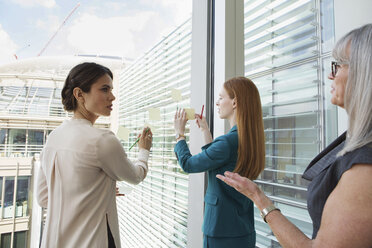 Businesswomen brainstorming ideas on glass window - CUF09020