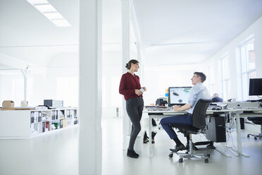 Colleagues in open plan office chatting - CUF09084