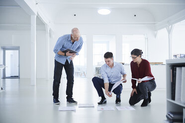 Colleagues working in open plan office looking at blueprints - CUF09102