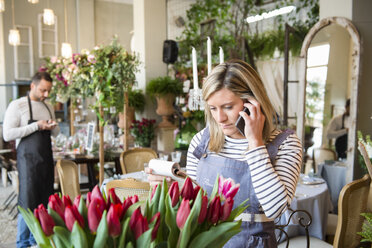 Florist im Blumenladen, der mit seinem Smartphone eine Blumenbestellung aufnimmt - CUF09127