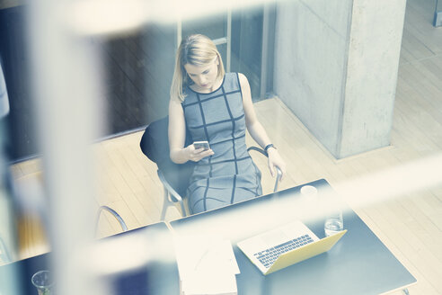 Hohe Winkel Fenster Ansicht der jungen Geschäftsfrau Blick auf Smartphone im Büro Schreibtisch - CUF09181